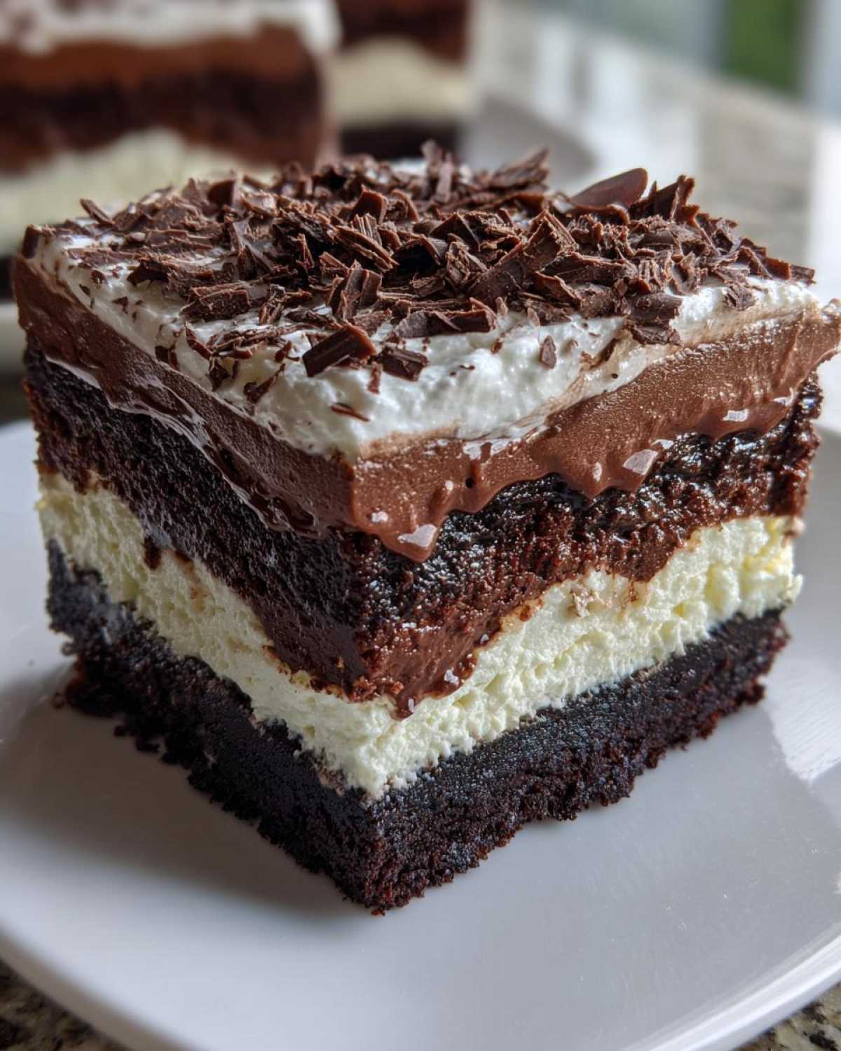 Close-up of a rich, layered brownie refrigerator cake slice topped with whipped cream and chocolate shavings.
