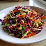 Close-up of a vibrant cabbage salad featuring shredded red and green cabbage and carrots tossed in a zesty dressing.