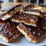 Close-up of stacked caramel ritz cracker christmas cookies topped with melted chocolate and flaky sea salt.