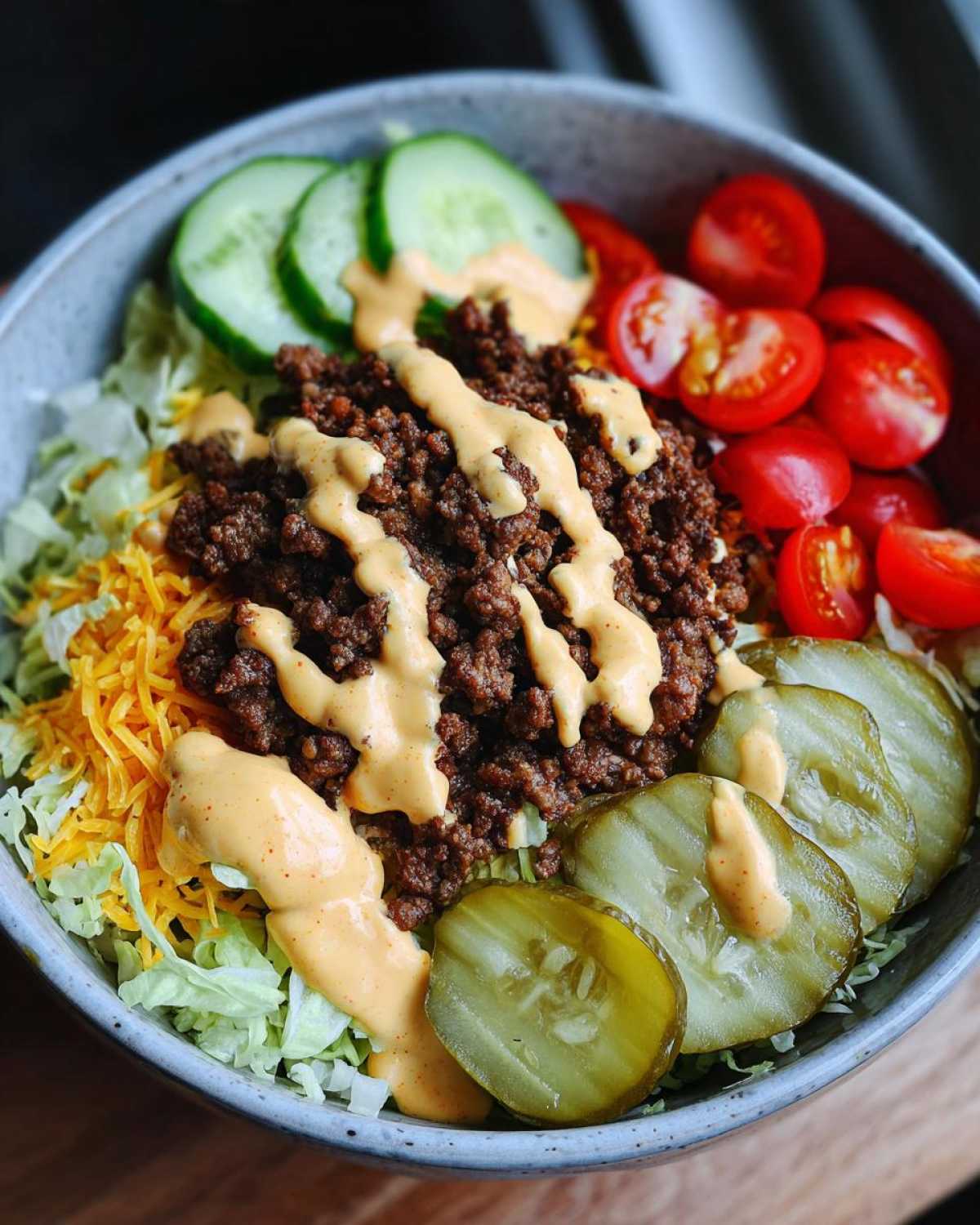 Close-up of a delicious cheeseburger bowl with seasoned ground beef, shredded lettuce, cheese, pickles, tomatoes, and special sauce.