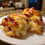 A close-up of a hearty slice of pierogi casserole topped with melted, browned cheese and bits of ham.