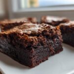 Close-up of a thick, chewy slice of dark chocolate gingerbread brownies on a white plate.
