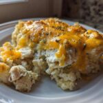 A close-up serving of creamy chicken cauliflower rice casserole topped with melted cheddar cheese and herbs.