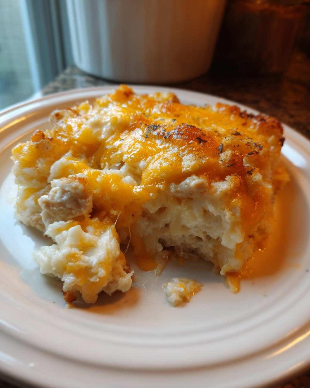 A close-up of a serving of chicken cauliflower rice casserole topped with melted cheddar cheese on a white plate.