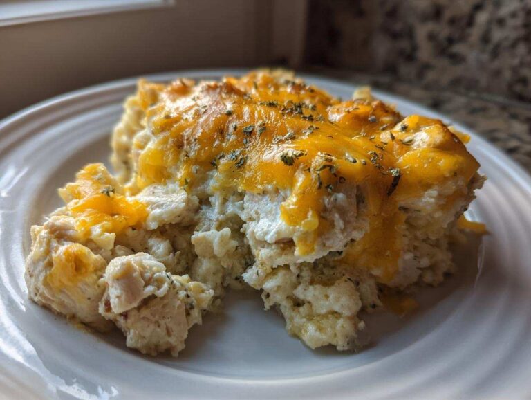 A close-up serving of creamy chicken cauliflower rice casserole topped with melted cheddar cheese and herbs.