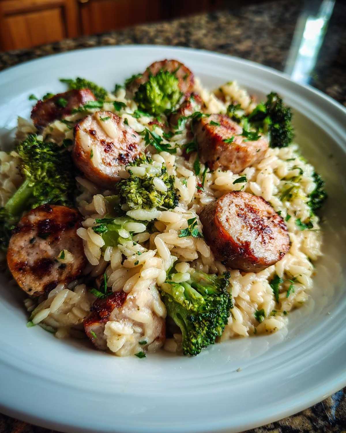 A close-up of a serving of creamy chicken sausage and broccoli orzo, garnished with fresh parsley.
