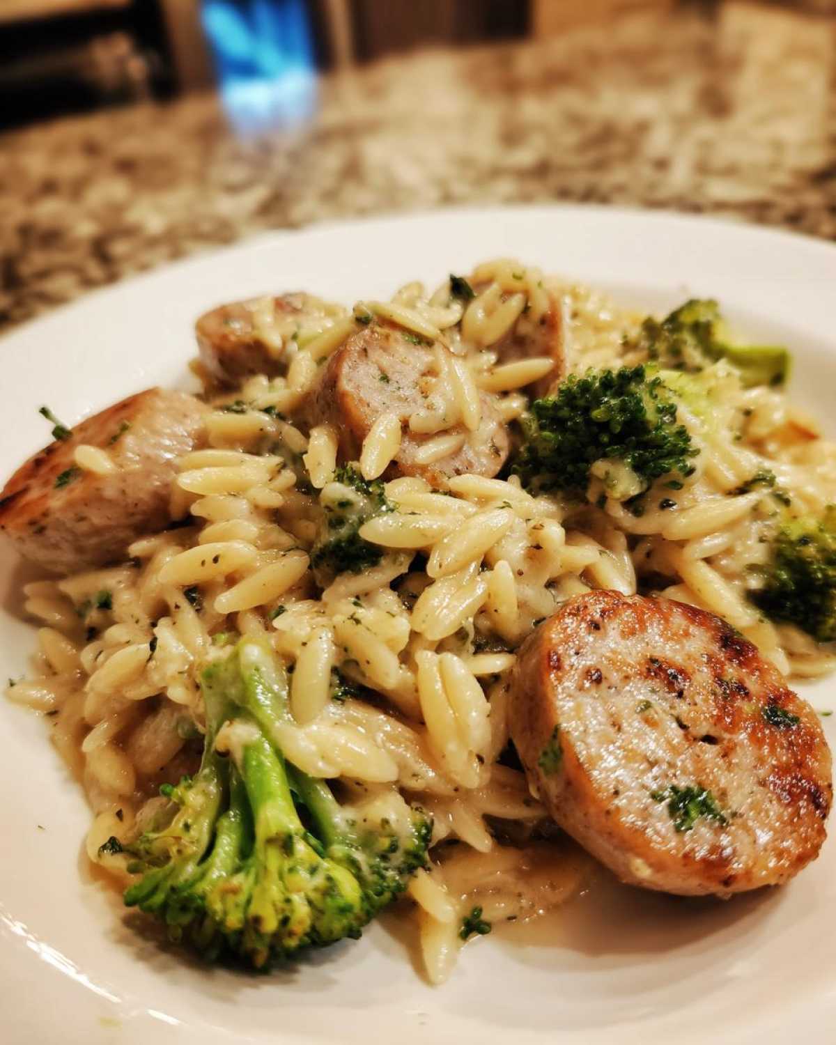 A close-up serving of creamy chicken sausage and broccoli orzo pasta on a white plate.