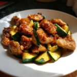 A close-up of glossy, glazed chicken pieces mixed with bright green zucchini slices in a chicken zucchini stir fry.
