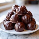 A tempting mound of homemade, dark chocolate-coated Oreo balls stacked on a white plate.
