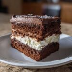 A rich, layered slice of chocolate italian love cake featuring dark cake, white cream filling, and chocolate frosting.