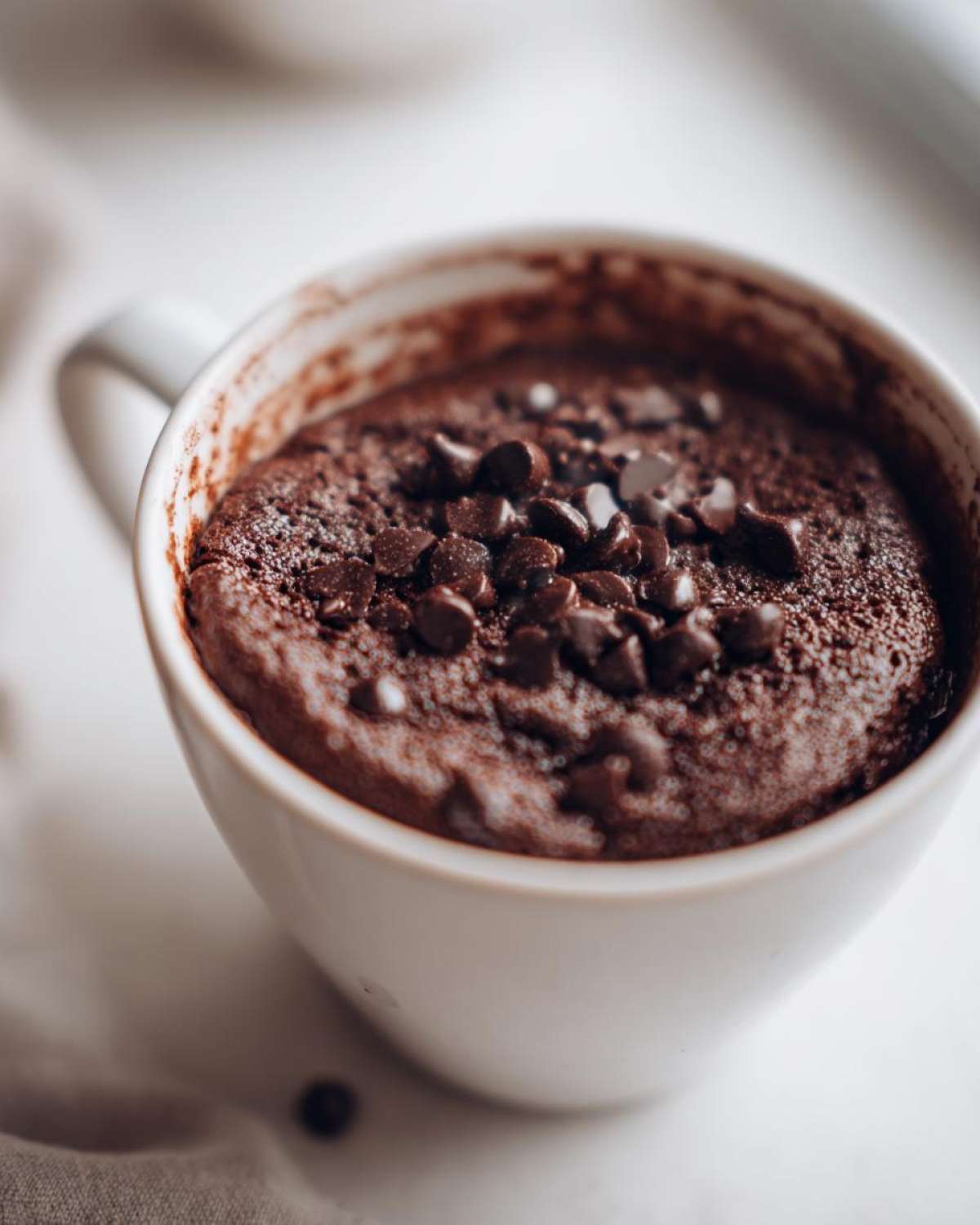 Close-up of a freshly baked chocolate mug cake topped generously with chocolate chips.