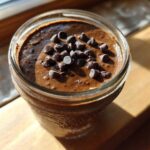 Overhead close-up of rich chocolate overnight oats topped with chocolate chips in a glass jar.