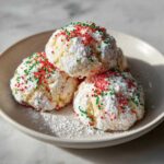 Close-up of three Christmas gooey butter cookies dusted with powdered sugar and red/green sprinkles.