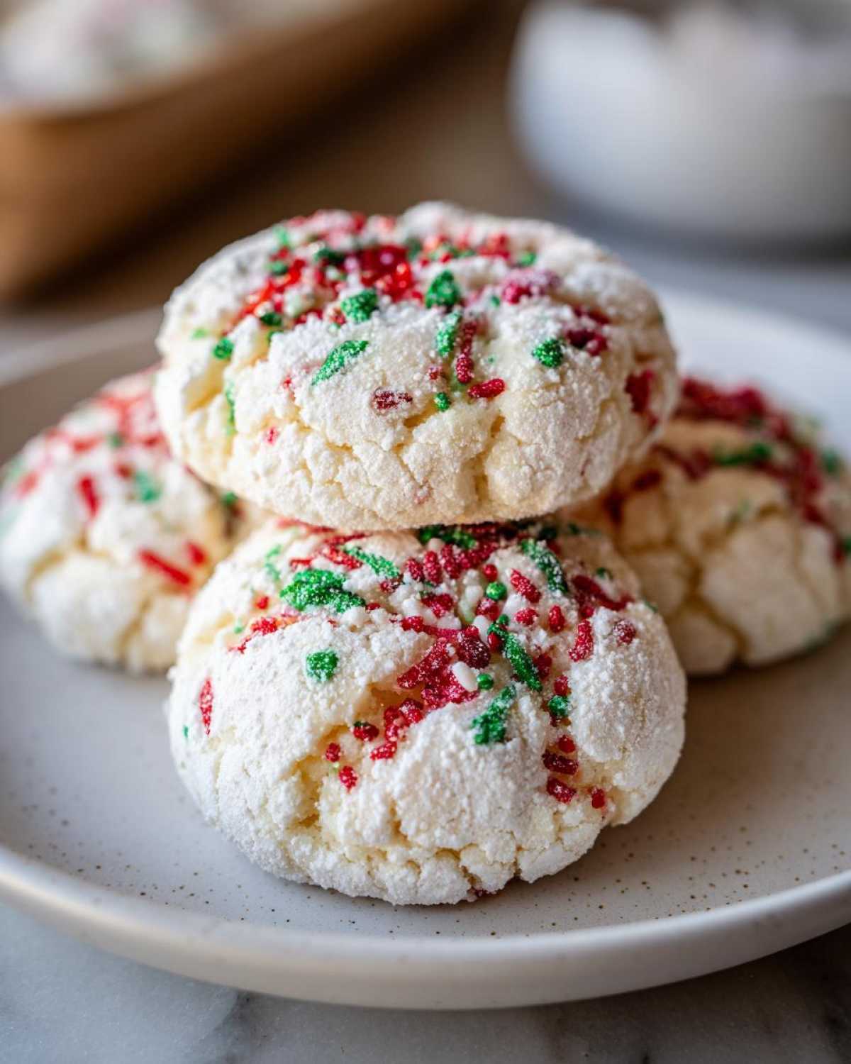 Close-up of stacked Christmas gooey butter cookies coated in powdered sugar and red and green sprinkles.