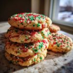 A stack of four soft, golden christmas sprinkle sugar cookies topped with red, green, and white nonpareils.