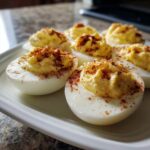 Close-up of several classic deviled eggs filled with creamy yolk mixture and sprinkled with paprika on a white platter.