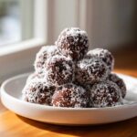 A mound of rich, dark bourbon balls generously coated in shredded coconut, served on a white dish.