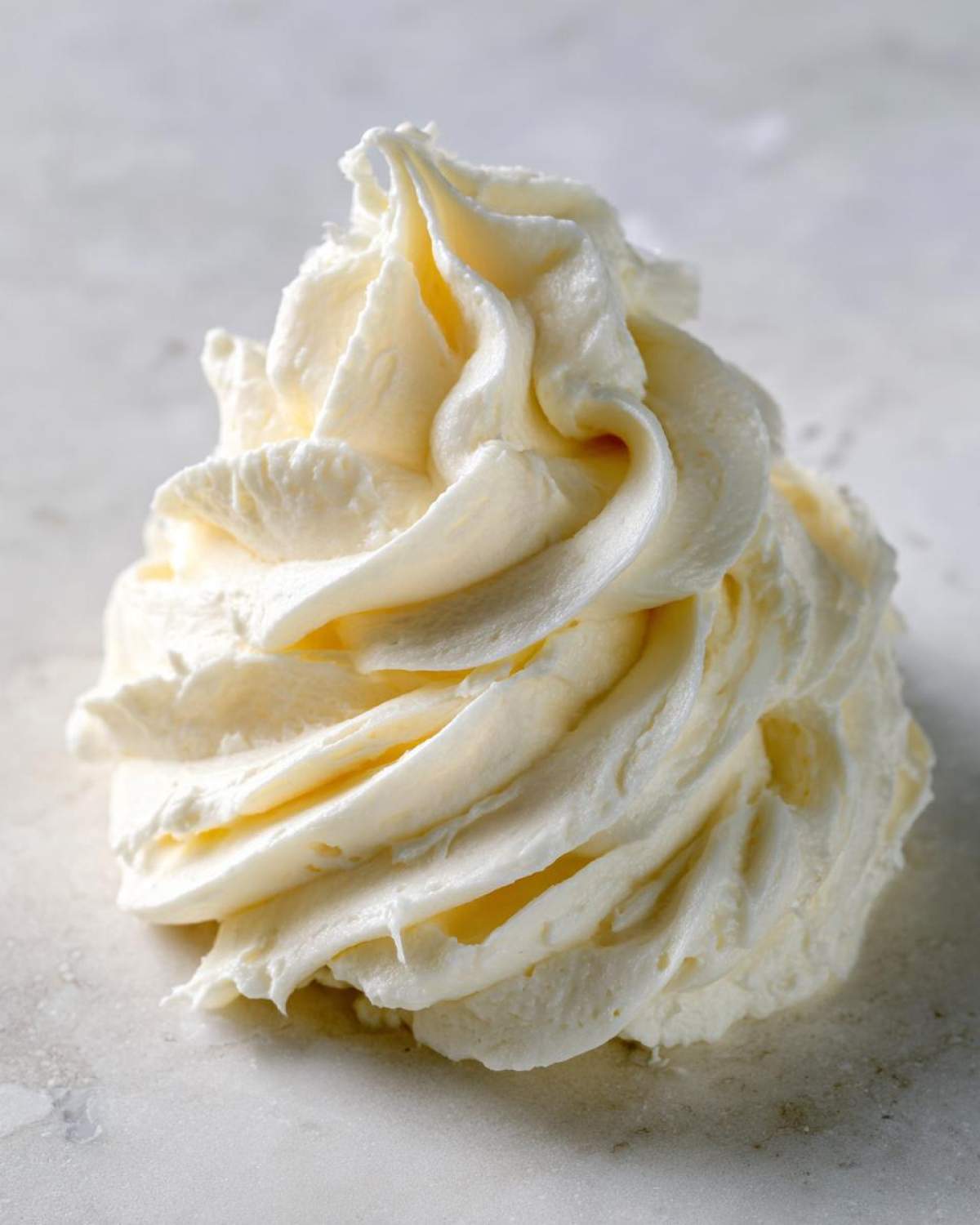 A beautiful, thick swirl of light yellow cream cheese frosting piped onto a light surface.