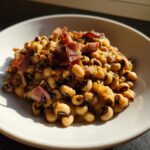 A close-up of creamy black eyed peas topped with crispy pieces of bacon served in a white bowl.