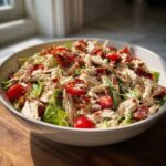 A large white bowl filled with creamy blt chicken salad featuring shredded chicken, lettuce, cherry tomatoes, and bacon crumbles.