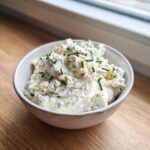 A small white bowl filled with chunky, creamy blue cheese dip, garnished with chopped green chives.