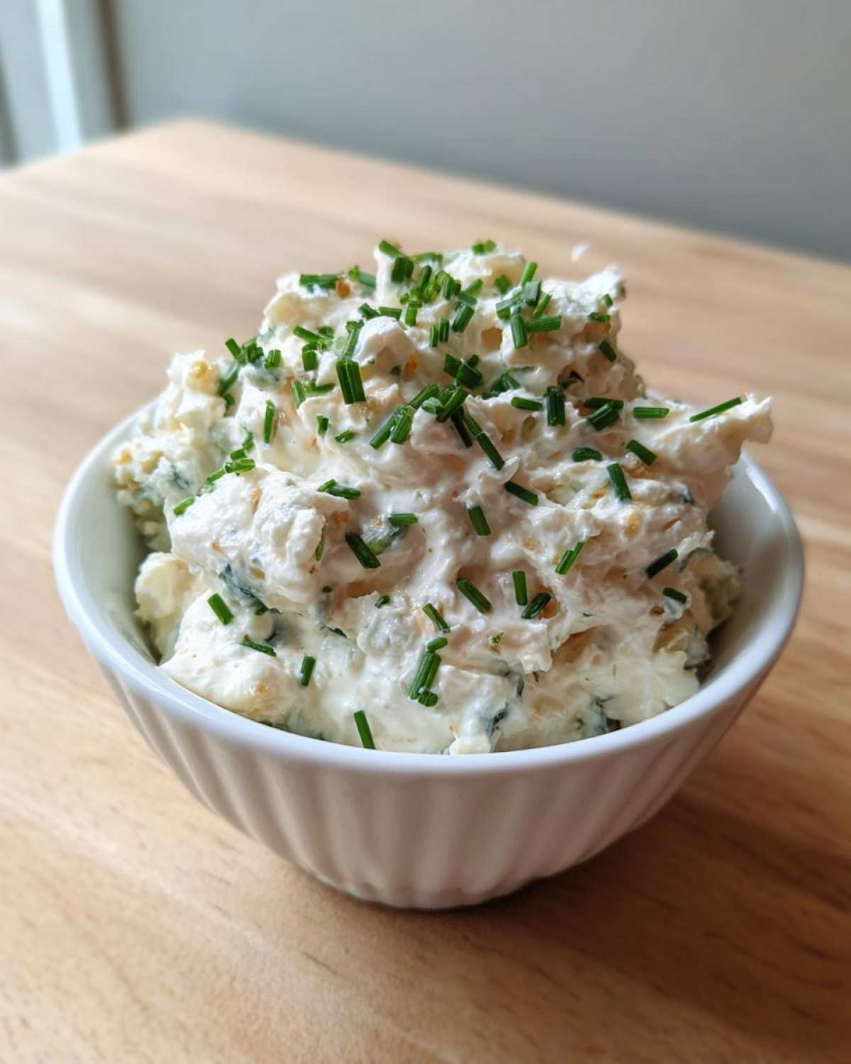 A white bowl filled with creamy, chunky blue cheese dip, garnished generously with chopped green chives.