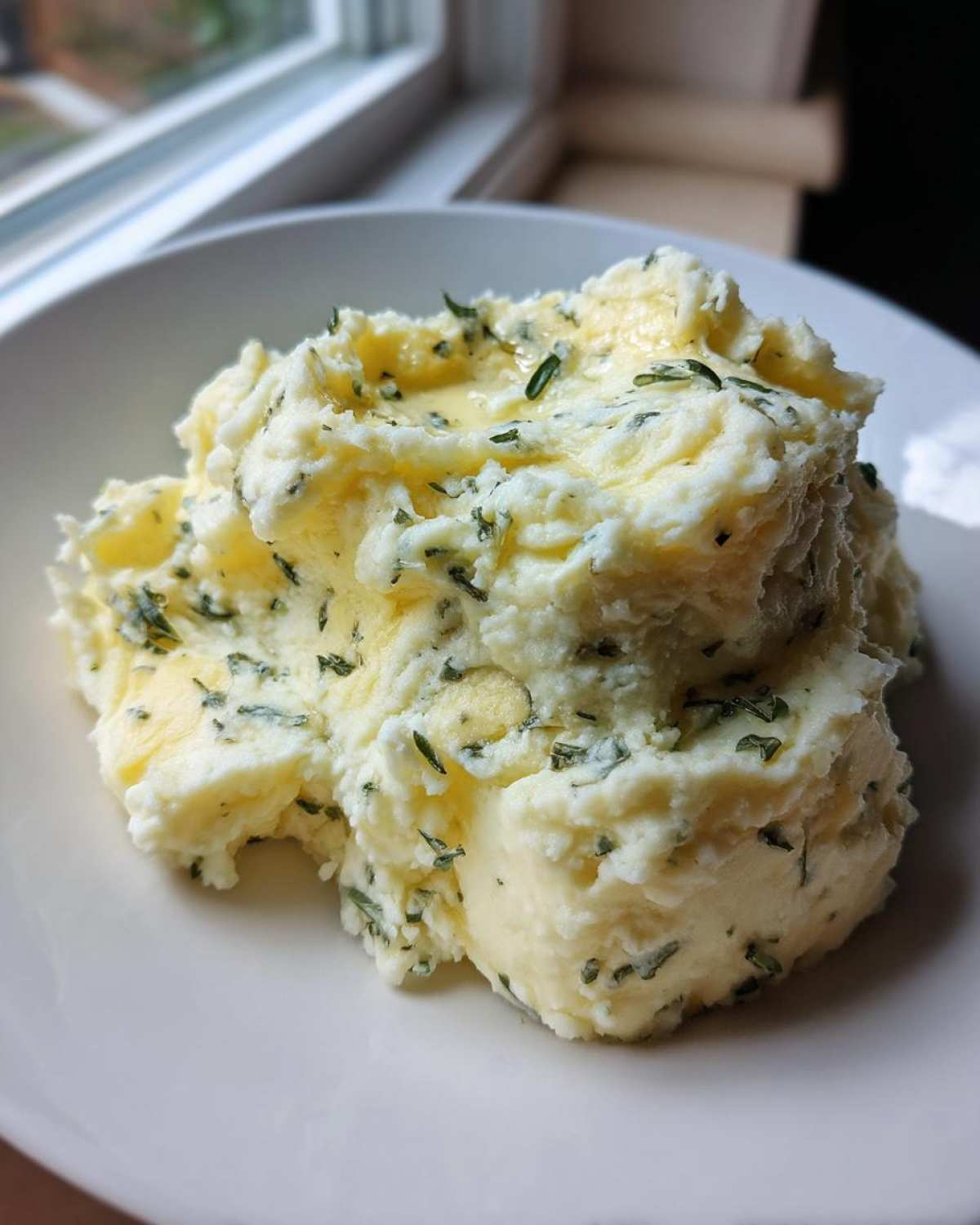 A close-up of creamy Boursin mashed potatoes topped with melted butter and fresh green herbs.
