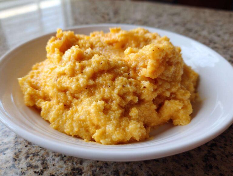 A close-up of rich, creamy, orange-yellow cheese grits served in a simple white bowl.