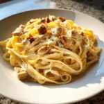 A close-up of creamy chicken fettuccine alfredo pasta topped with grilled chicken pieces and grated cheese.
