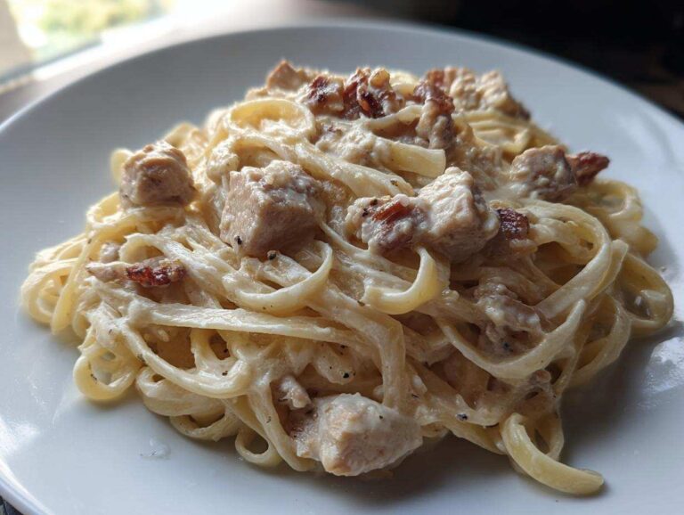 Close-up of creamy chicken fettuccine alfredo pasta tossed in a rich white sauce with visible chunks of chicken.