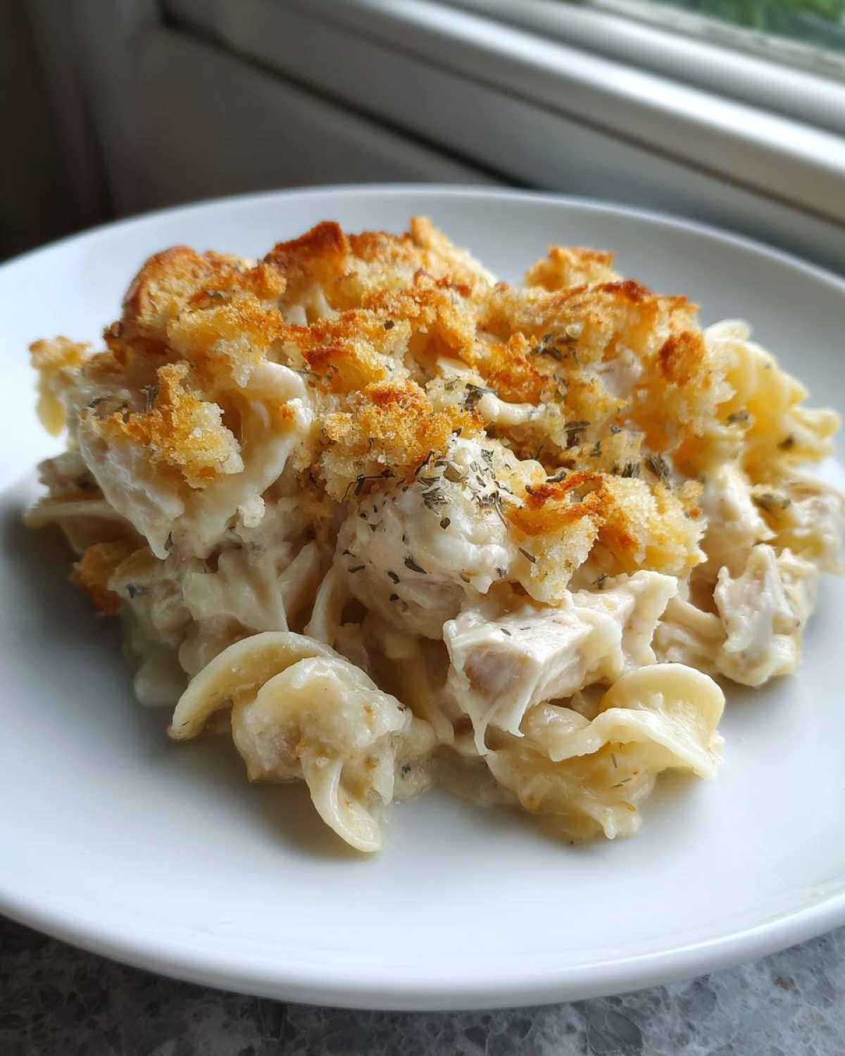 A close-up serving of creamy chicken noodle casserole topped with golden brown breadcrumbs and herbs.