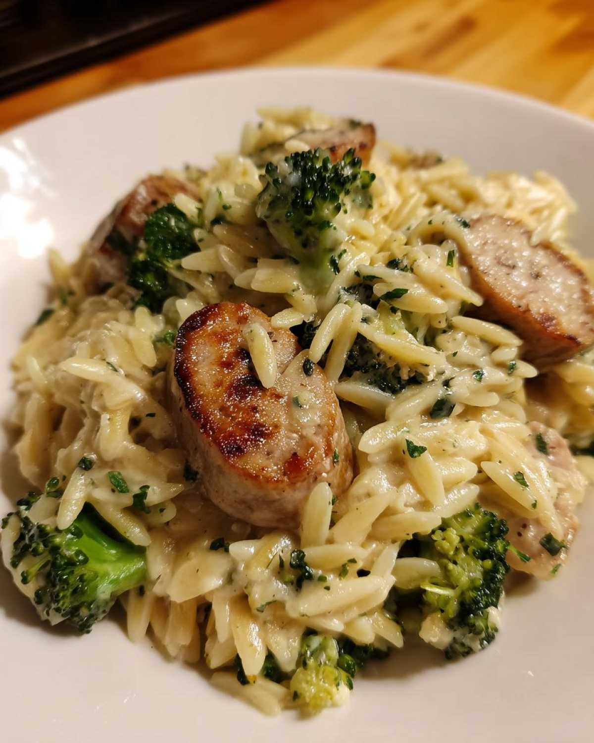 Close-up of a creamy bowl of chicken sausage and broccoli orzo pasta, garnished with fresh herbs.