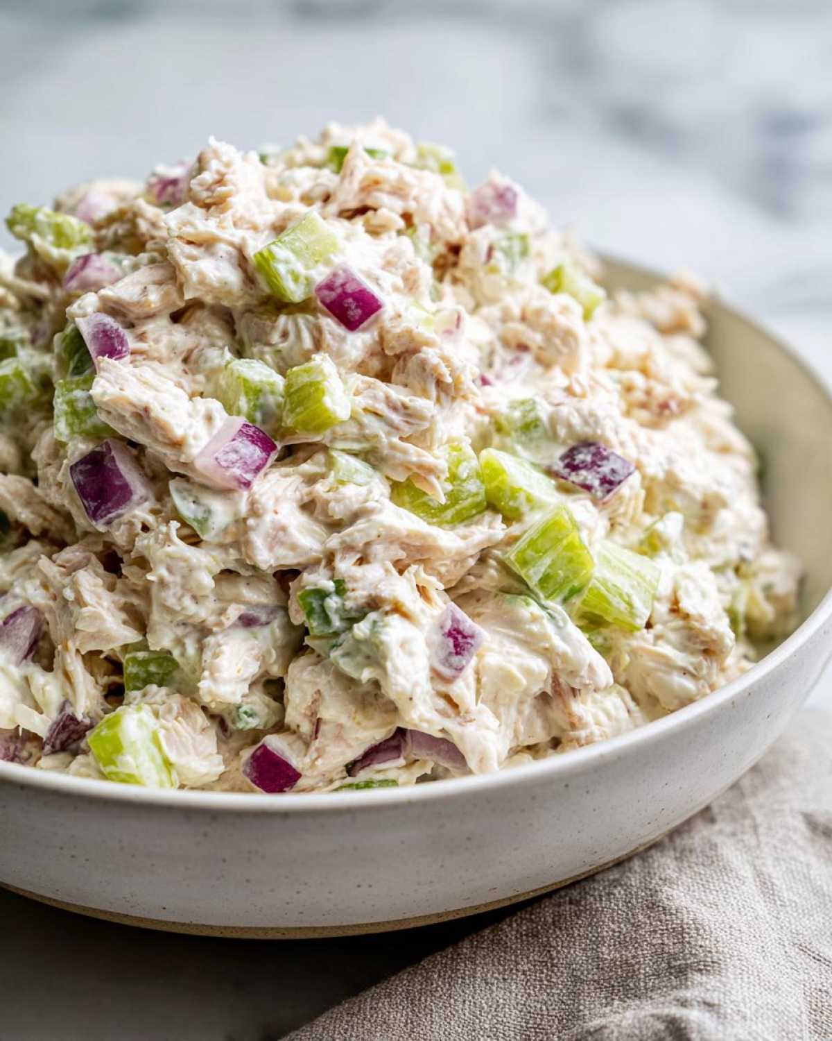 A close-up of creamy cottage cheese chicken salad mixed with chunks of celery and red onion in a white bowl.