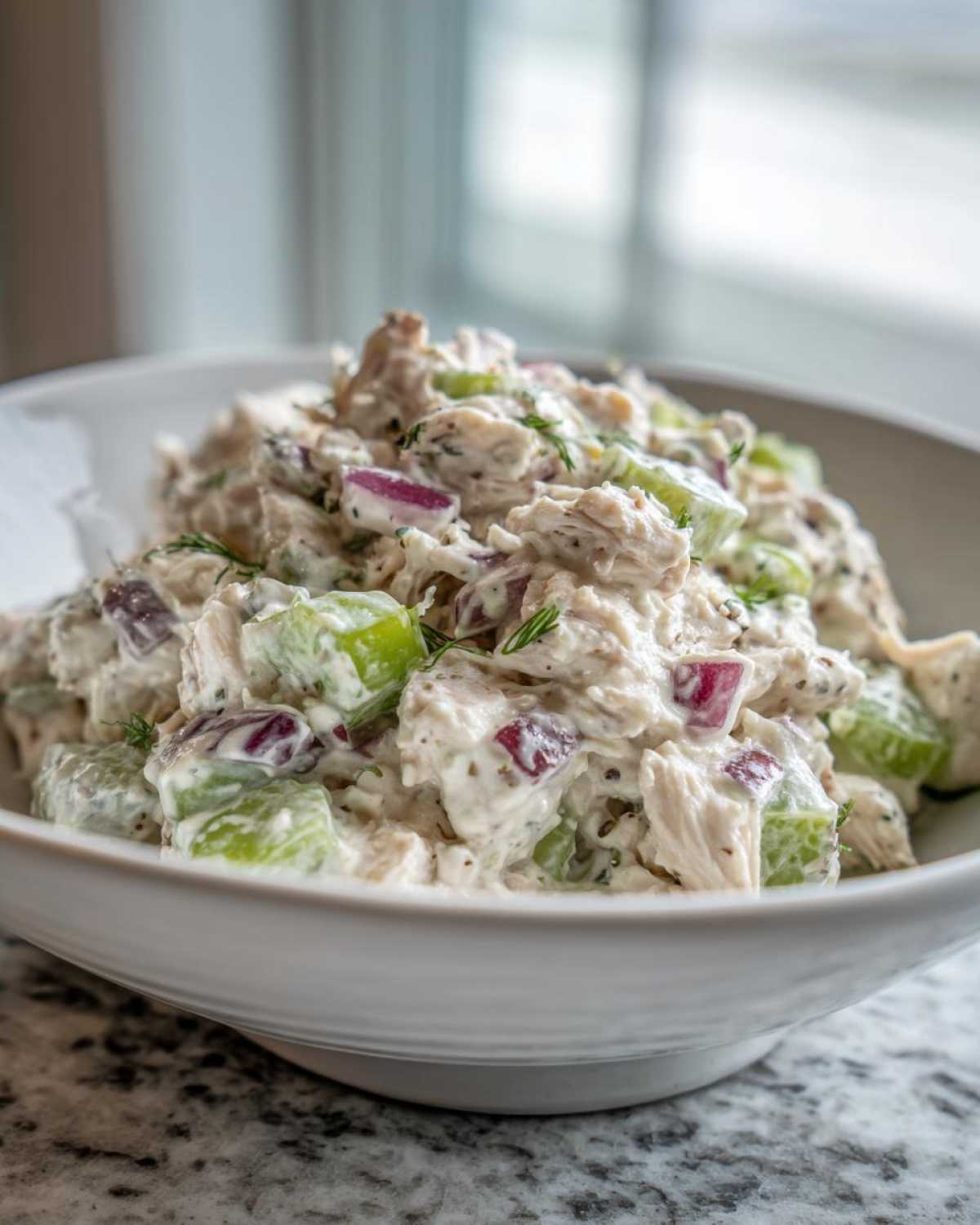 A close-up of creamy cottage cheese chicken salad mixed with celery and red onion in a white bowl.
