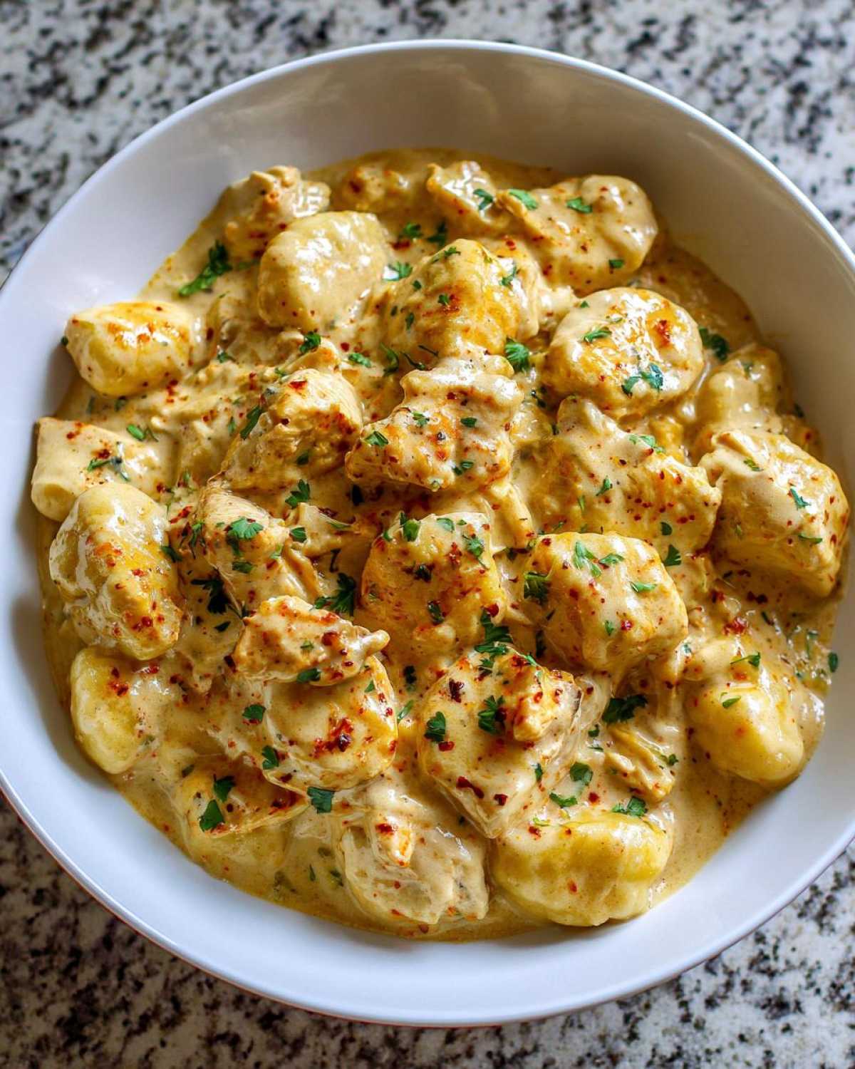 Close-up of creamy crack chicken gnocchi dish served in a white bowl, garnished with parsley.