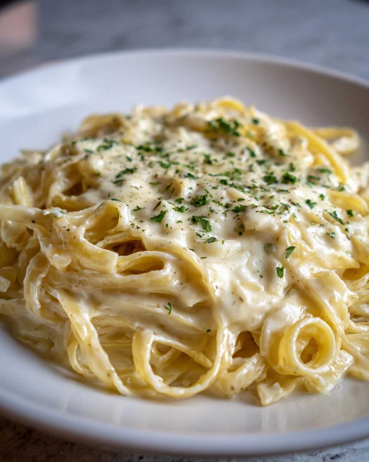 Close-up of fettuccine pasta generously coated in creamy Olive Garden Alfredo Sauce and topped with parsley.