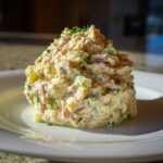 A perfectly molded mound of creamy ham salad recipe, featuring visible chunks of ham and celery, garnished with fresh herbs.