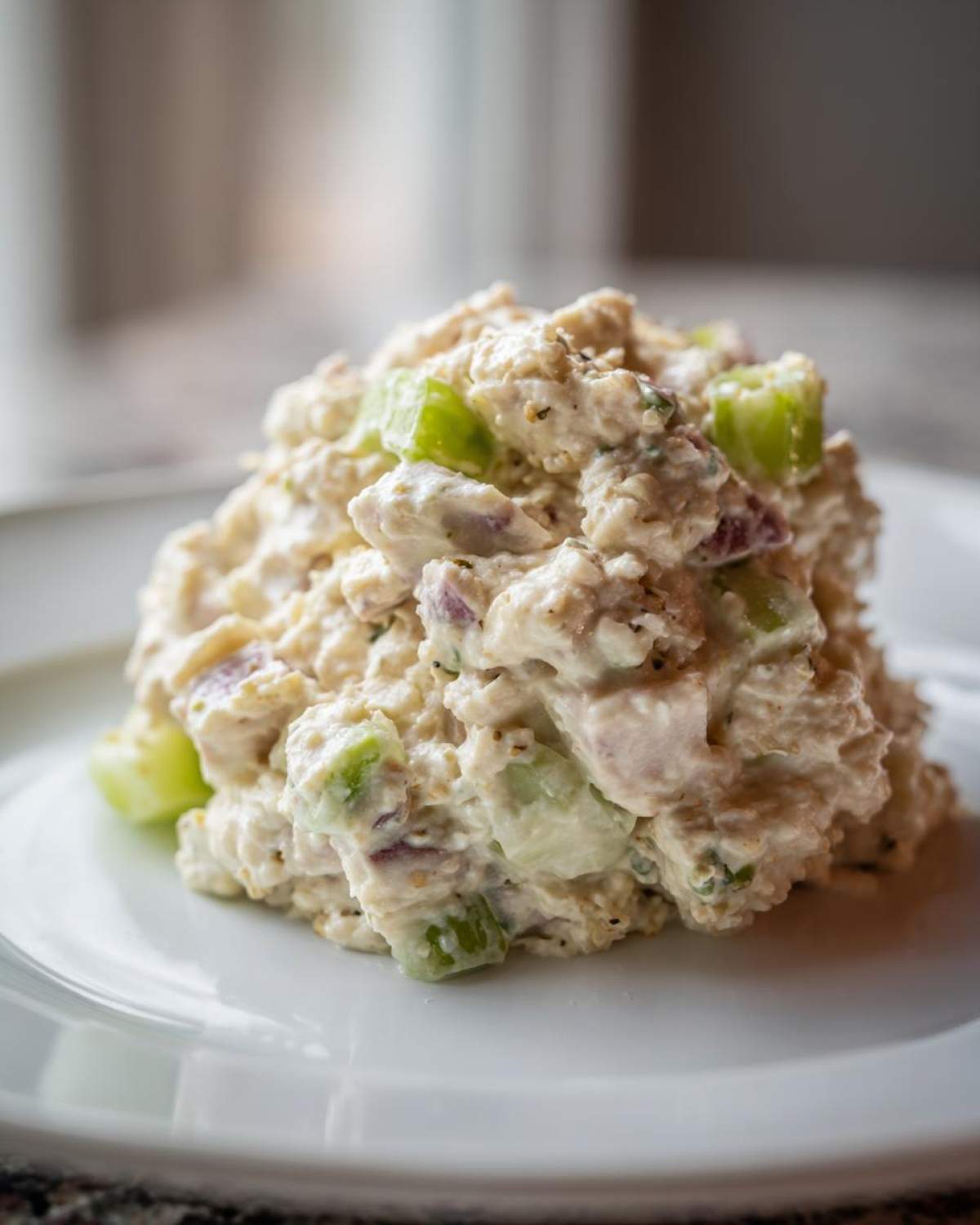 A mound of creamy ham salad recipe mixed with diced celery and red onion on a white plate.