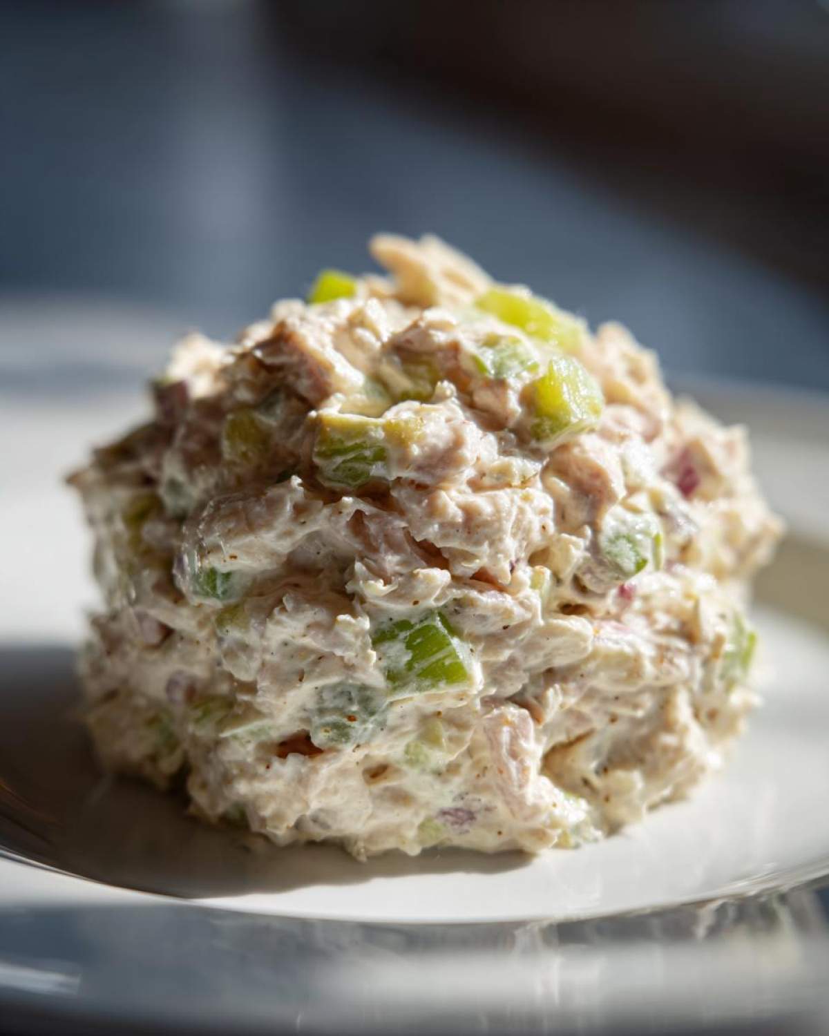 A scoop of creamy ham salad recipe mixed with green celery and red onion on a white plate.