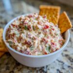 Close-up of creamy hoagie dip loaded with meat and vegetables, served in a white bowl with crackers.