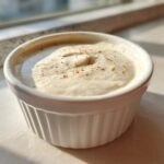 A close-up of thick, creamy horseradish sauce sprinkled with pepper in a small white fluted ramekin.