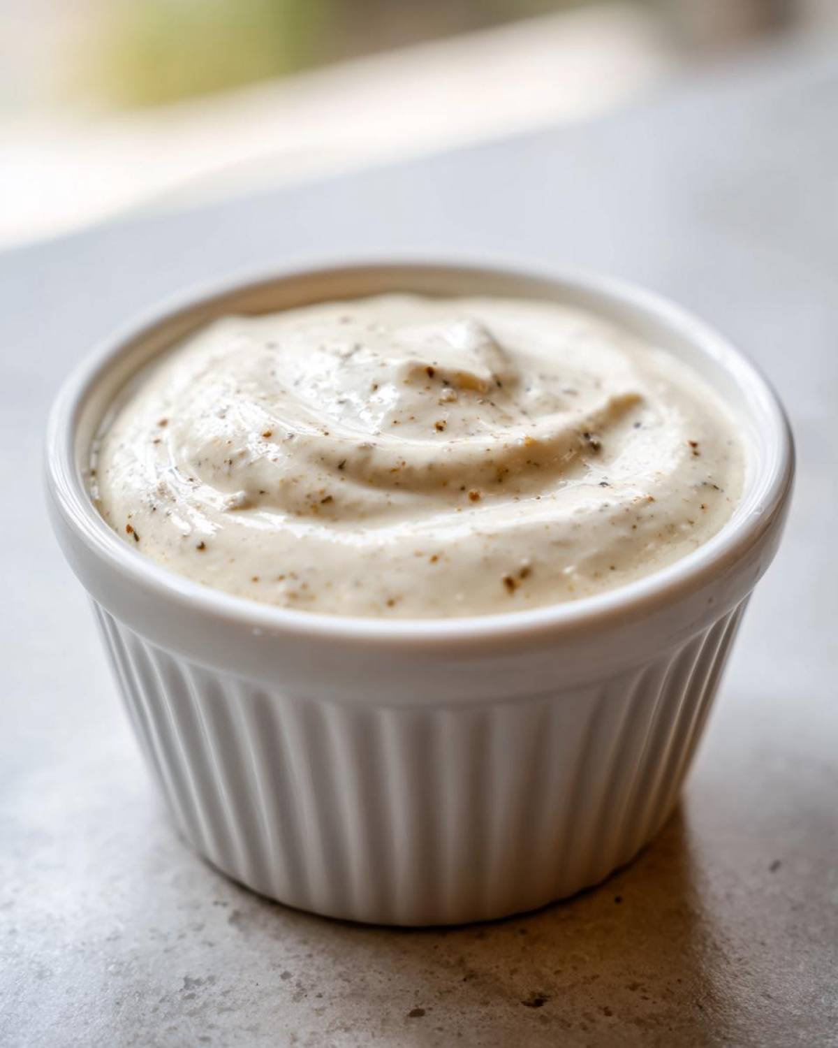 A close-up of thick, creamy horseradish sauce speckled with pepper in a small white fluted ramekin.