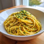 A close-up of a white bowl filled with bright yellow Creamy Lemon Pasta, topped generously with lemon zest and fresh chopped parsley.