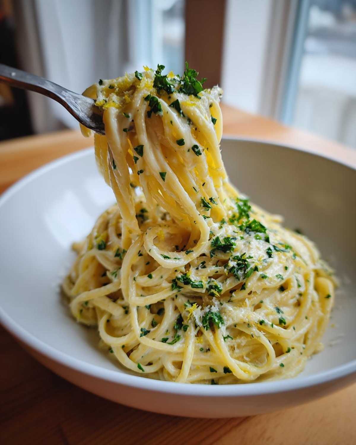 A fork lifts a twirl of Creamy Lemon Pasta coated in sauce, garnished with lemon zest and fresh parsley.