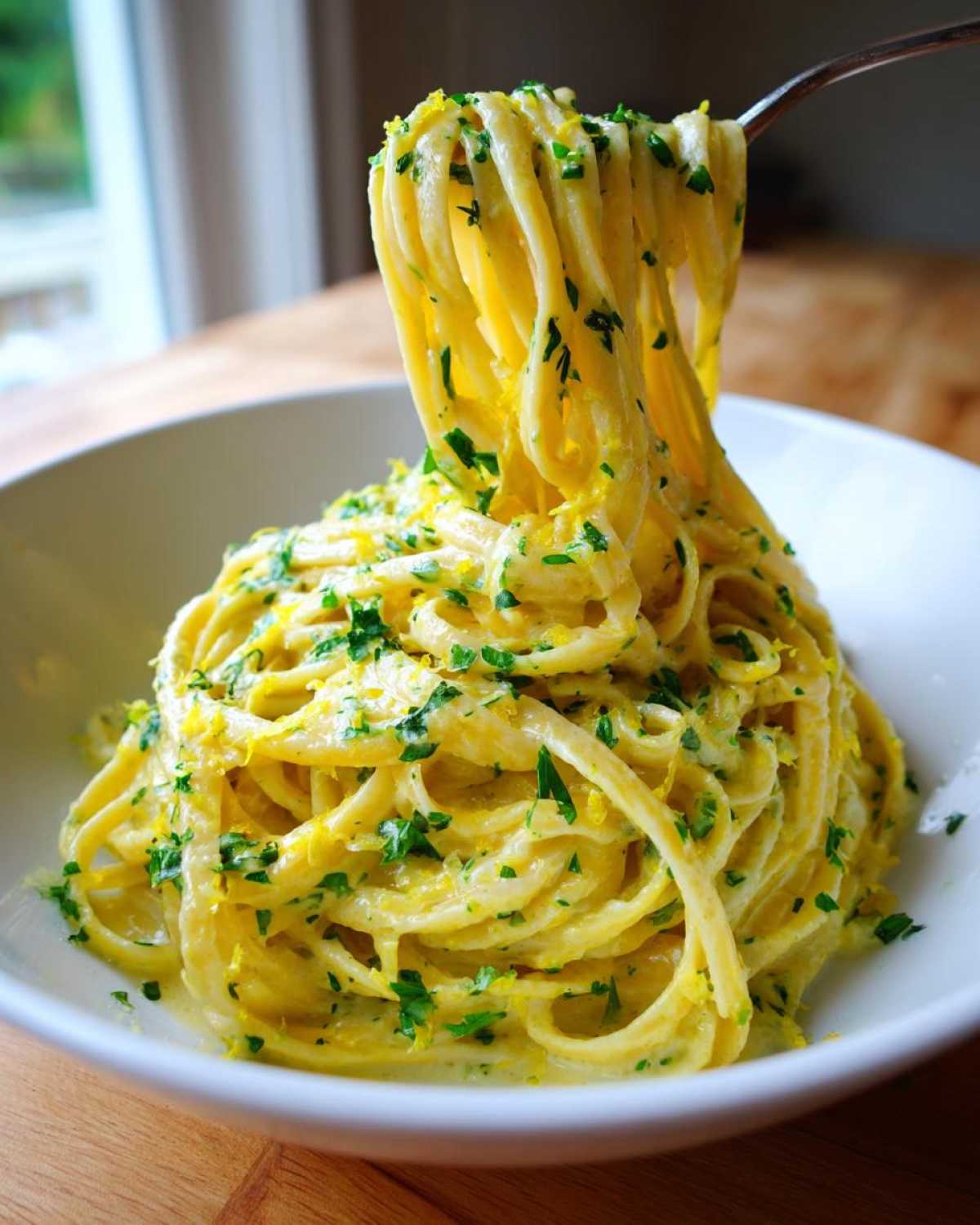 A fork lifts a generous twirl of linguine coated in rich sauce, showcasing the bright zest and parsley of the Creamy Lemon Pasta.