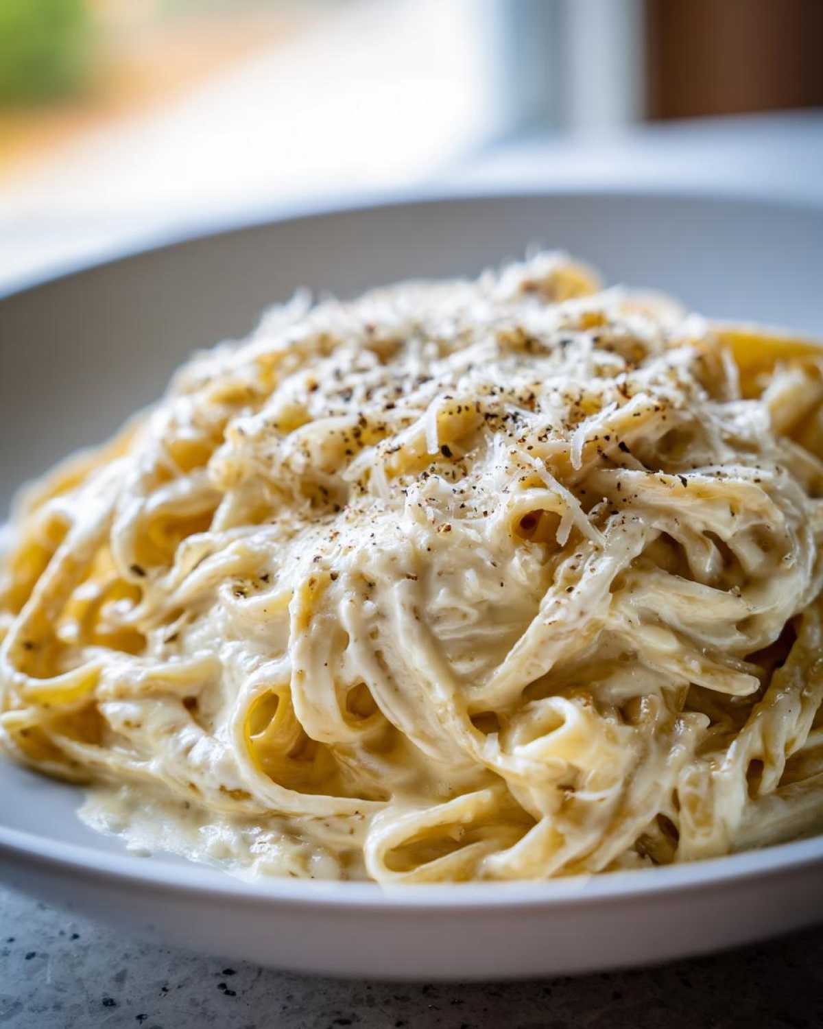 Close-up of fettuccine pasta coated in rich, creamy Olive Garden Alfredo Sauce, topped with Parmesan and black pepper.