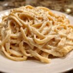 A close-up of fettuccine pasta generously coated in creamy Olive Garden Alfredo Sauce and topped with black pepper.