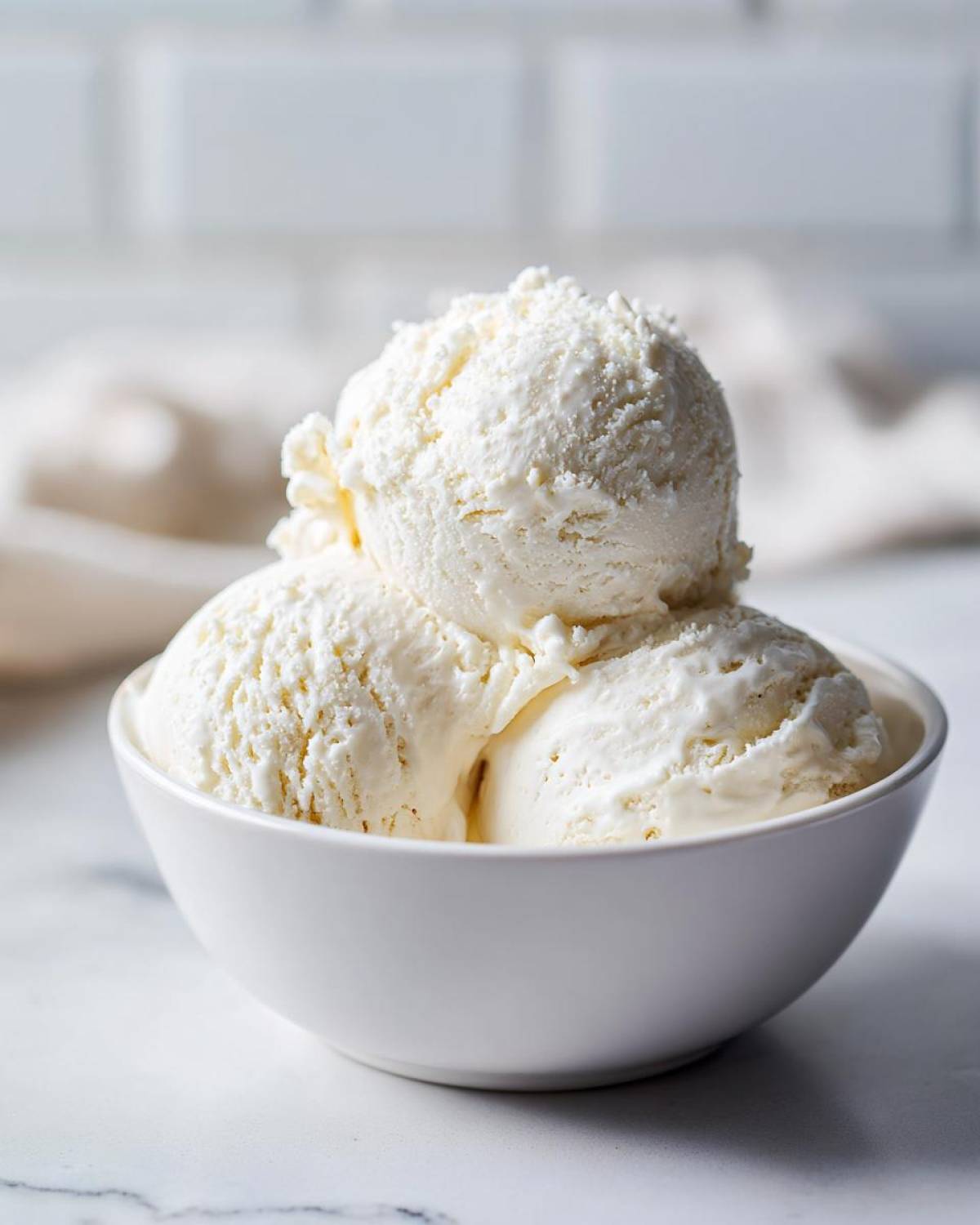Three scoops of creamy vanilla protein ice cream served in a small white bowl on a marble surface.