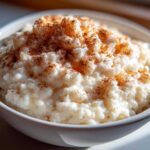 Close-up of creamy rice pudding in a white bowl, generously sprinkled with cinnamon.