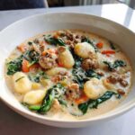 A close-up of a hearty bowl of creamy sausage gnocchi soup with spinach and carrots.
